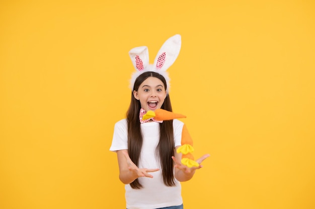 La ragazza sorpresa del bambino di pasqua con le orecchie da coniglio e il farfallino tiene la carota buona pasqua