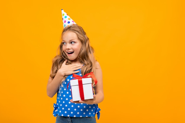 La ragazza sorpresa in un cappello di festa tiene un contenitore di regalo