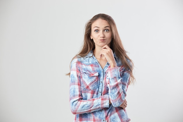 La ragazza sorpresa vestita con una camicia a scacchi si erge sullo sfondo bianco in studio