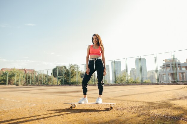 La ragazza sorridente cavalca sul longboard sul vecchio campo da tennis