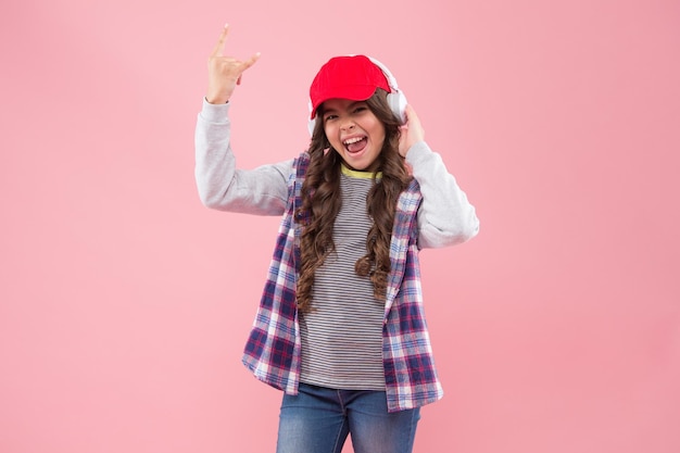 La ragazza sorridente del bambino in stile casual ascolta la canzone preferita in cuffia moderna divertendosi