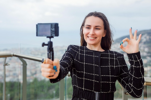 La ragazza sorridente del blogger sta facendo un selfie mostrando un gesto ok sullo sfondo della vista sulla città