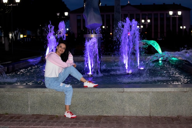 La ragazza sorridente felice si siede alla fontana di notte