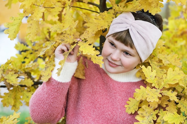 La ragazza sorridente guarda dalle foglie gialle della quercia in autunno all'aperto