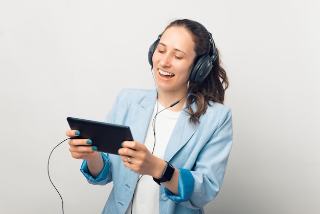 La ragazza sorridente indossa le cuffie e guarda o suona qualcosa sul tablet che tiene in mano.