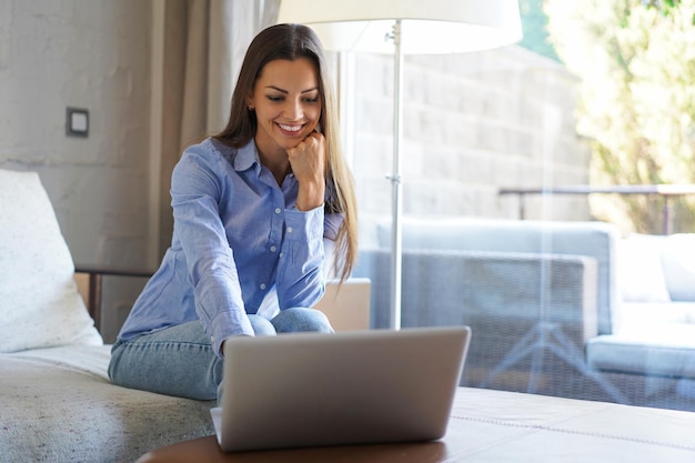 La ragazza sorridente si siede sul divano a guardare il webinar sul laptop Felice giovane donna studia sul corso online a distanza