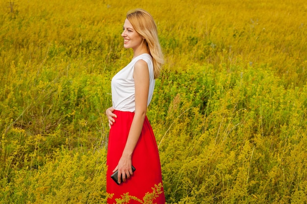 La ragazza sorridente si trova in un campo di fiori gialli e posa davanti a una macchina fotografica