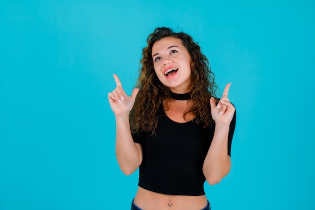 La ragazza sorridente sta alzando lo sguardo e indicando in su con gli indici su fondo blu