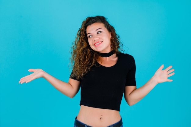 La ragazza sorridente sta guardando a sinistra aprendo le mani su sfondo blu