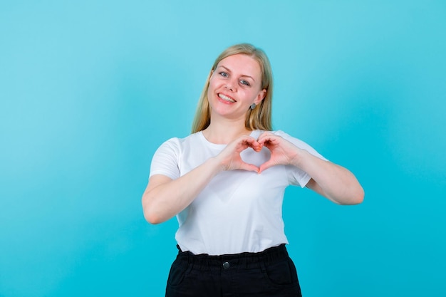 La ragazza sorridente sta mostrando il gesto del cuore su sfondo blu