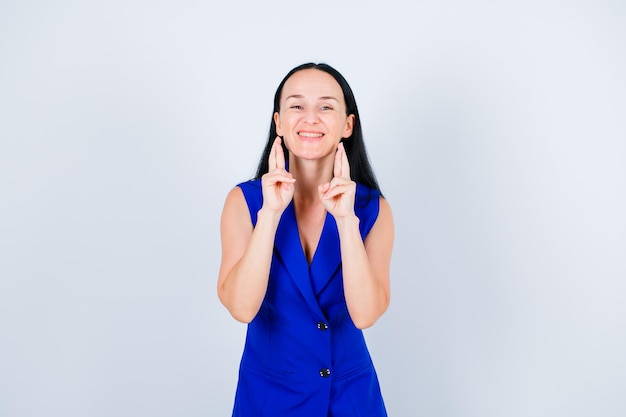 La ragazza sorridente sta mostrando le dita incrociate su priorità bassa bianca