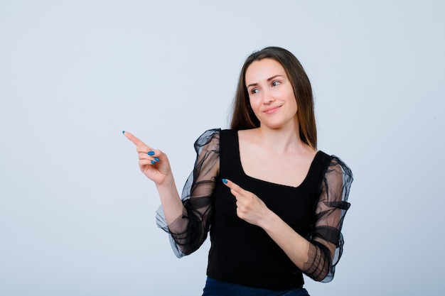 La ragazza sorridente sta puntando a sinistra con gli indici su sfondo bianco