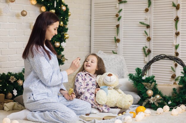 La ragazza sorridente sveglia del bambino con sua madre gioca con l'orsacchiotto a casa. Natale