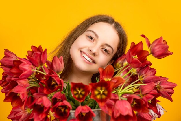 La ragazza sorridente tiene i fiori del tulipano della molla su fondo giallo