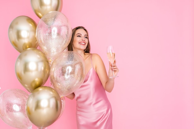 La ragazza sorridente tiene le mongolfiere dello champagne sulla festa di festa di compleanno del nuovo anno di sfondo colorato
