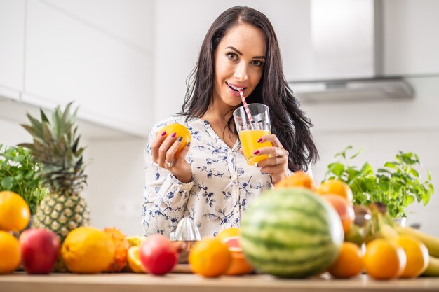 La ragazza sorseggia un succo d'arancia appena spremuto con una cannuccia di carta circondata da un assortimento di frutta.