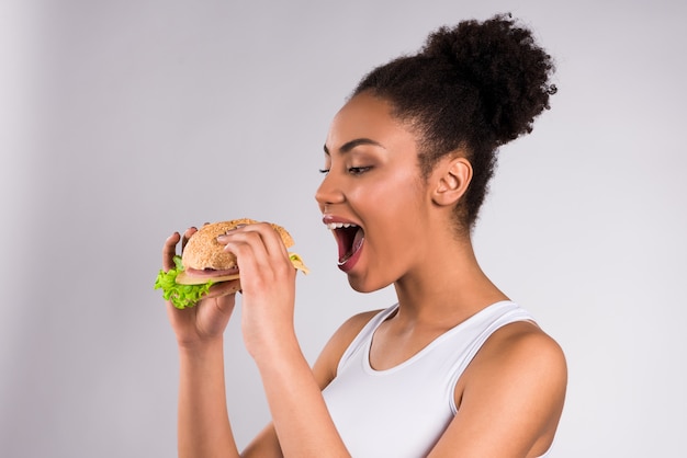 La ragazza spalanca la bocca per mangiare un grande hamburger.