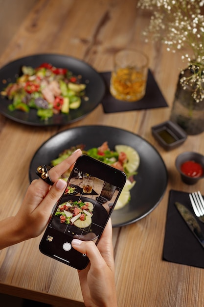 La ragazza spara la tavola apparecchiata nel ristorante sul suo smartphone un tavolo di legno da tavola nero in prima persona