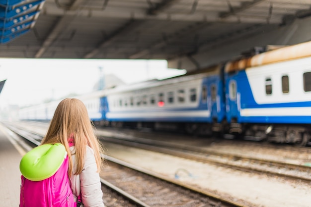 La ragazza sta aspettando il treno. Ragazza con uno zaino e con cuscino verde del collo