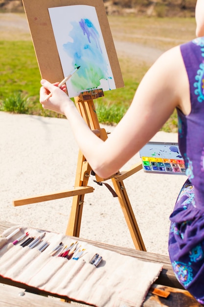 La ragazza sta dipingendo con acquerello sul cavalletto all'aperto Immaginazione primaverile Artista che lavora alla pittura nel parco primaverile