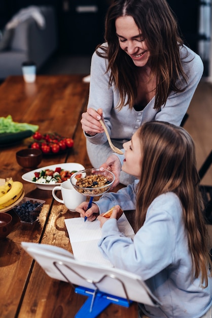 La ragazza sta facendo i compiti al tavolo della cucina e sua madre le dà un assaggio di cibo.