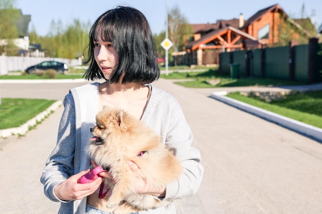 La ragazza sta giocando abbracciando tenendo per mano il suo simpatico cane Spitz Pomerania seduto su un prato verde all'aperto in un parco al giorno d'estate Giovane donna che cammina con buffo cucciolo soffice Amore animale domestico