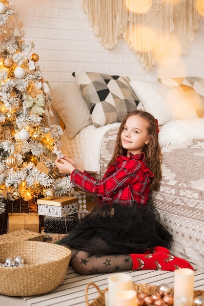 La ragazza sta guardando le decorazioni di Natale. Indossa abiti a quadri rossi e un fiocco tra i capelli. Preparazione per il nuovo anno.