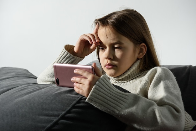 La ragazza sta guardando lo schermo di uno smartphone appoggiato al cuscino di un divano.