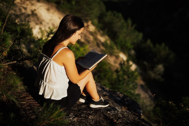 La ragazza sta leggendo il libro, mentre è seduto contro uno splendido scenario naturale.