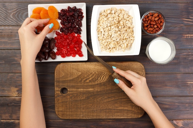 La ragazza sta preparando la colazione. Tagliare la frutta secca in porridge di farina d'avena su un tagliere. Colazione utile e salutare. sfondo in legno scuro, vista dall'alto.