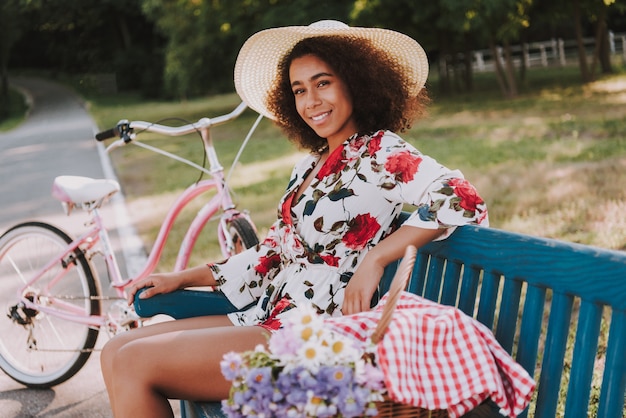 La ragazza sta sedendosi sulla panchina del parco accanto alla bicicletta.