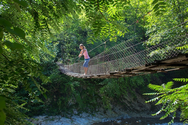 La ragazza sta sul ponte di legno sospeso attraverso il fiume della montagna e distoglie lo sguardo