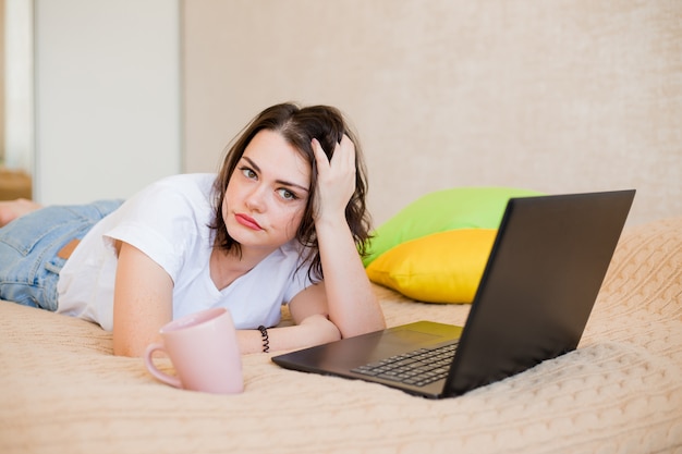 La ragazza sta trovandosi a casa su un letto con caffè e un computer portatile