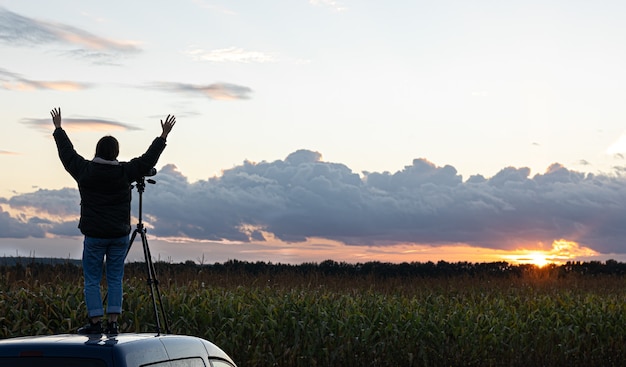 La ragazza sul tetto dell'auto fotografa il tramonto con un treppiede.