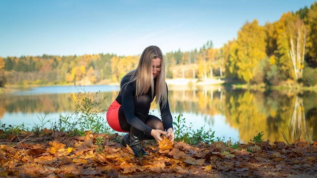 La ragazza sulla riva del serbatoio in autunno raccoglie le foglie gialle Concetto di spazio