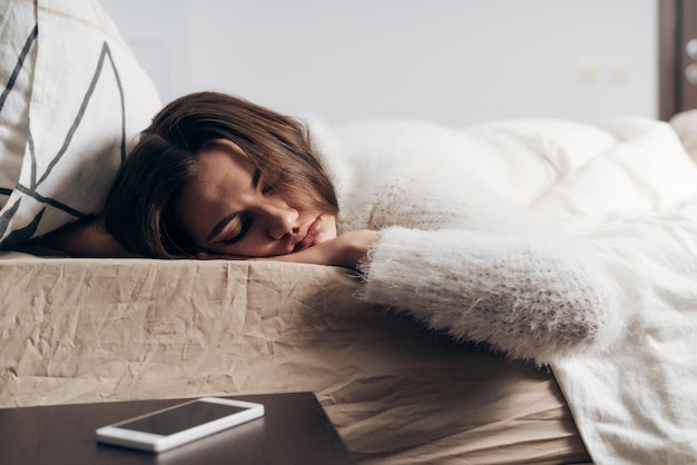 La ragazza sveglia in pigiama bianco che dorme sul letto la mattina presto non può sentire la sveglia