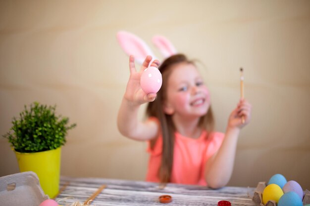 La ragazza sveglia nelle orecchie del coniglietto di pasqua che dipinge le uova di pasqua a casa si prepara al fuoco selettivo di pasqua