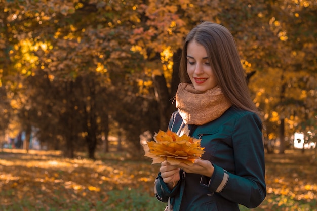 La ragazza sveglia sta nel parco e guarda le foglie nelle mani di