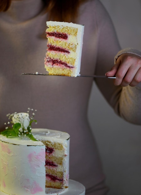 La ragazza taglia e serve un pezzo di torta festosa torta a due livelli decorata con fiori freschi su sfondo grigio