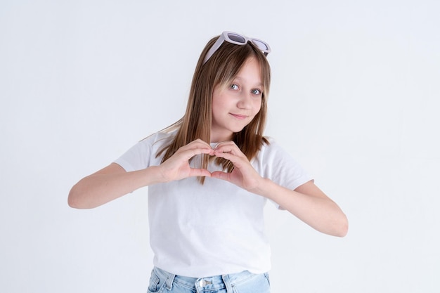 La ragazza teenager alla moda mostra una forma del cuore con le sue dita e sorride