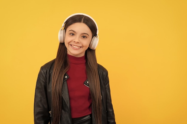 La ragazza teenager felice ascolta la musica nelle cuffie su fondo giallo con la musica dello spazio della copia