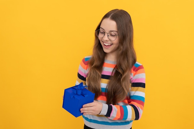 La ragazza teenager felice in occhiali tiene la scatola del regalo per lo shopping natalizio