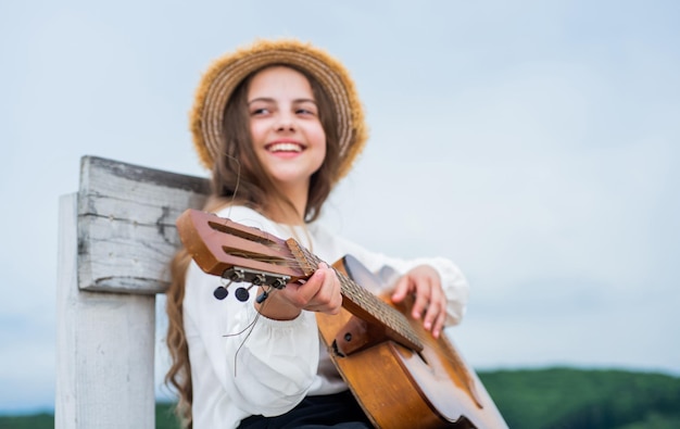 La ragazza teenager felice suona la chitarra acustica all'aperto sul musicista di sfondo del cielo