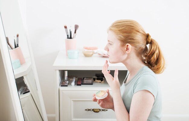 La ragazza teenager ha dipinto l'acne sul fronte davanti allo specchio