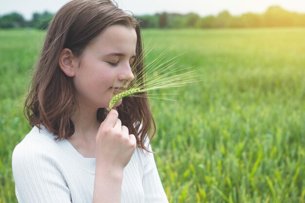 La ragazza teenager tocca le mani con grano verde nel campo