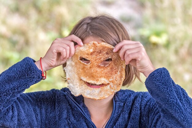 La ragazza tiene il pancake con le fessure come maschera e copre il viso da esso