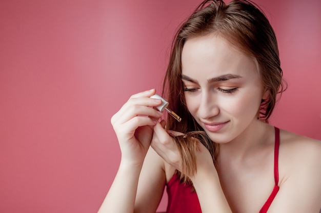 La ragazza tiene in mano le punte dei capelli e la mano destra le applica olio giallo.