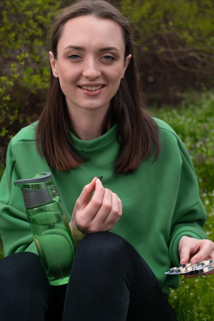 La ragazza tiene in mano le vitamine e imbottiglia in primavera nella foresta vestita con una giacca verde