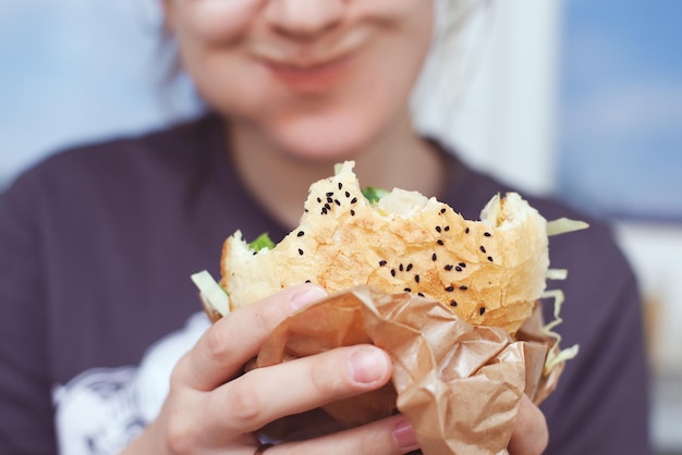 La ragazza tiene in mano un grosso hamburger. Sfondo sfocato morbido. stile di vita