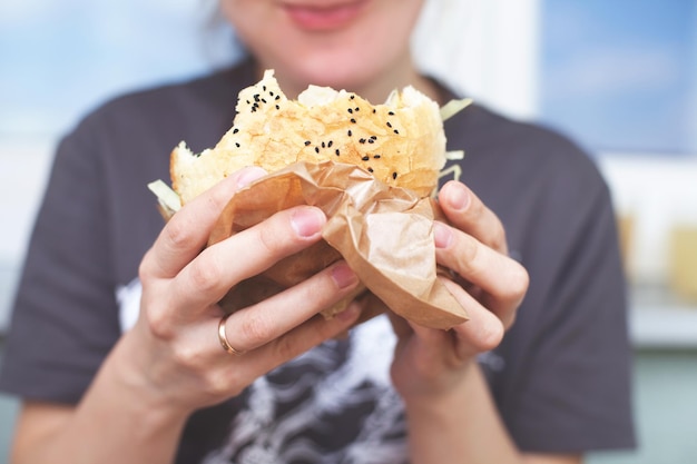 La ragazza tiene in mano un grosso hamburger. Sfondo sfocato morbido. stile di vita